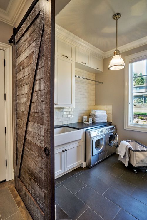 Rustic laundry room featuring a sliding barn door, gray tile floors, stainless steel appliances, white