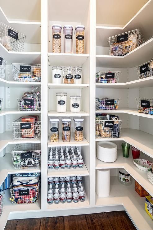 White u-shaped kitchen pantry boasts white modular shelves stocked with labeled wire snack baskets and cereal canisters.